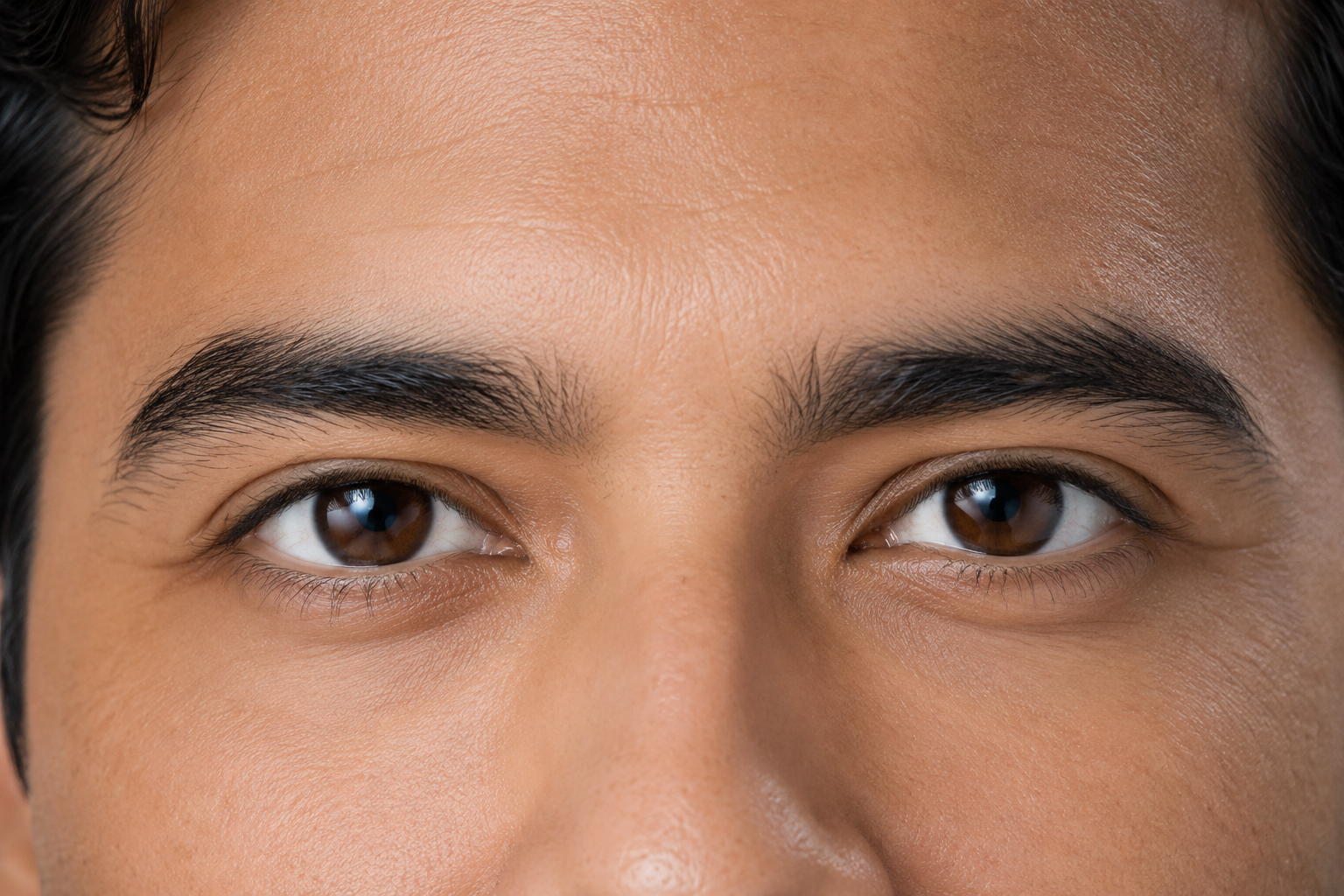 A tight crop showing ONLY the eyes and upper cheeks of a real actor (site-owned) producing a social, mouth-only smile. Lower lid flat and unengaged, no cheek lift, no crow’s feet, no bunching of skin beneath the eye. The mouth must be entirely outside the crop. Caption tag: the fake smile.