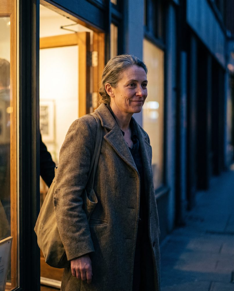 A woman in her late forties leaving an evening acting class, bag over one shoulder