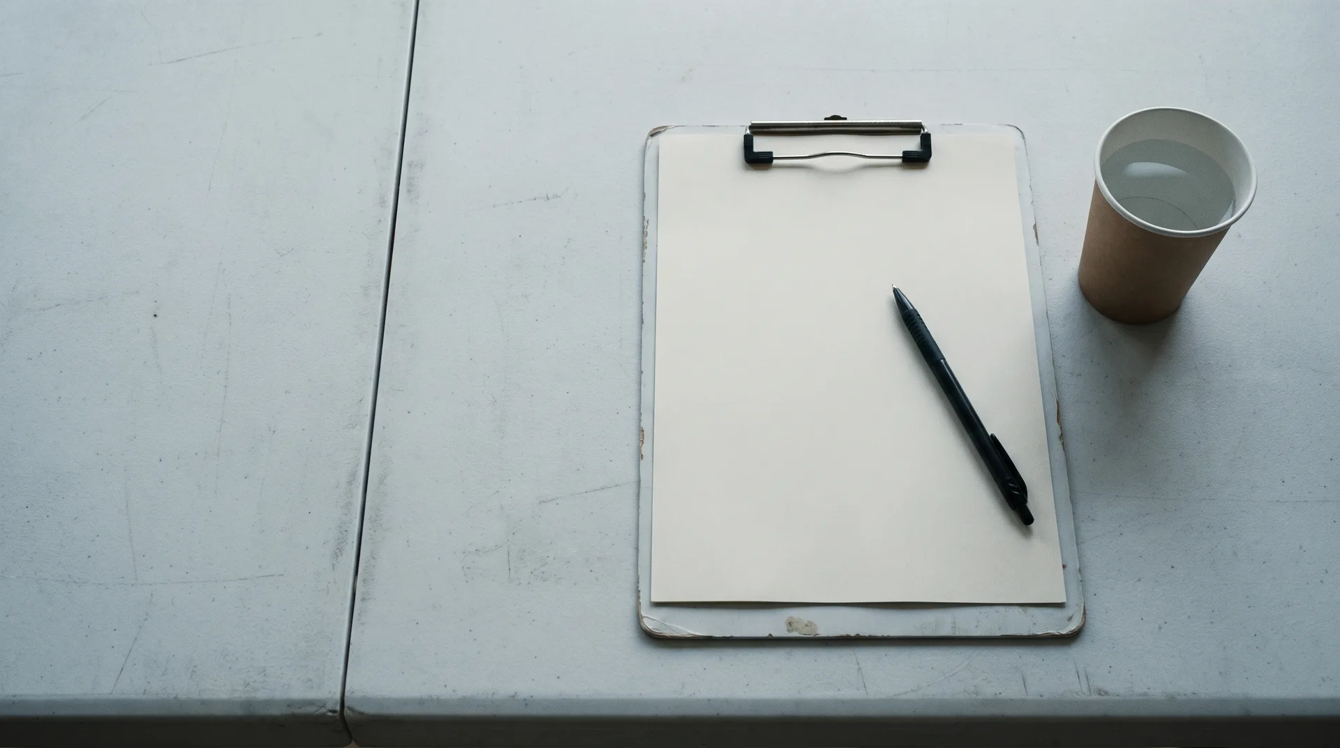 A clipboard with a blank sheet, a pen and a paper cup on a folding table