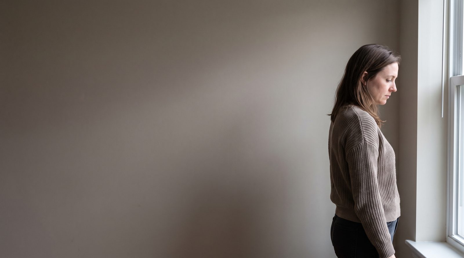 An actor standing in a plain room, caught in a private thought before speaking