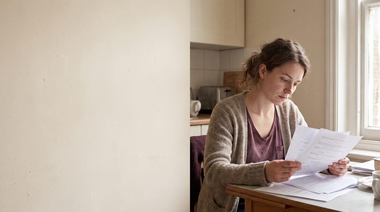 A woman at a kitchen table reading a few pages of a script