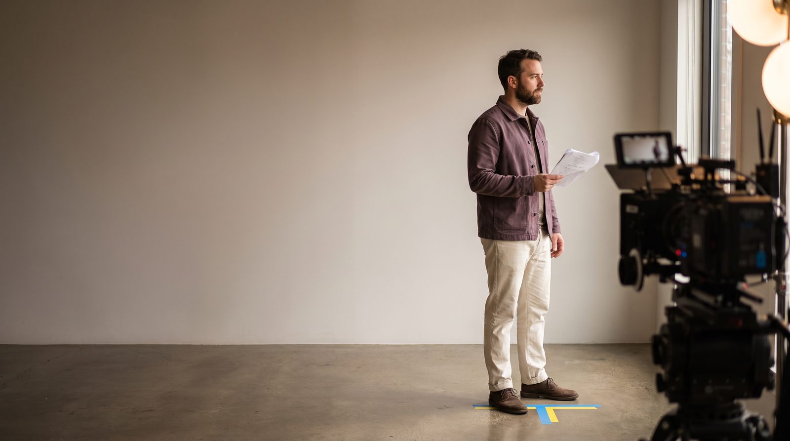 An actor standing on a taped mark on a film set, waiting between takes