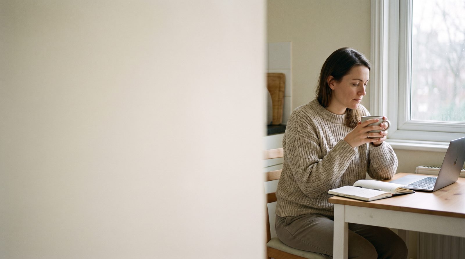 An actor sitting at a kitchen table in the early morning with a laptop, a diary and a cup of tea