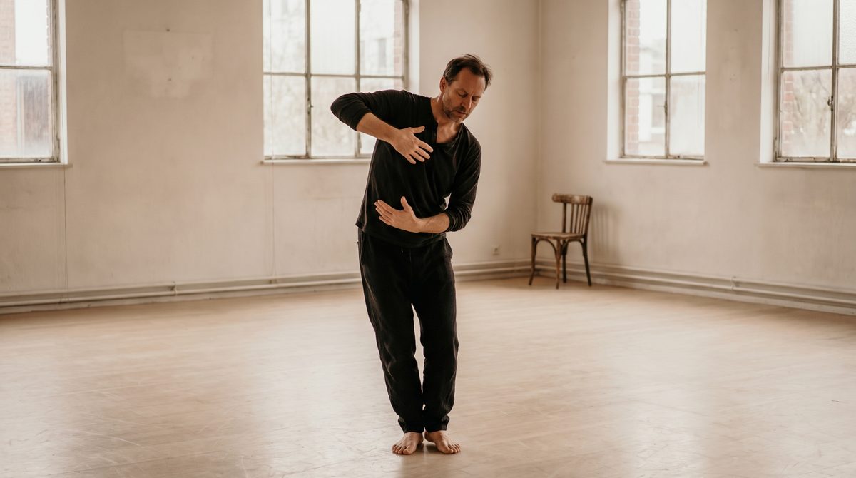 An actor mid-movement in an empty rehearsal room, arms extended in a large reaching action