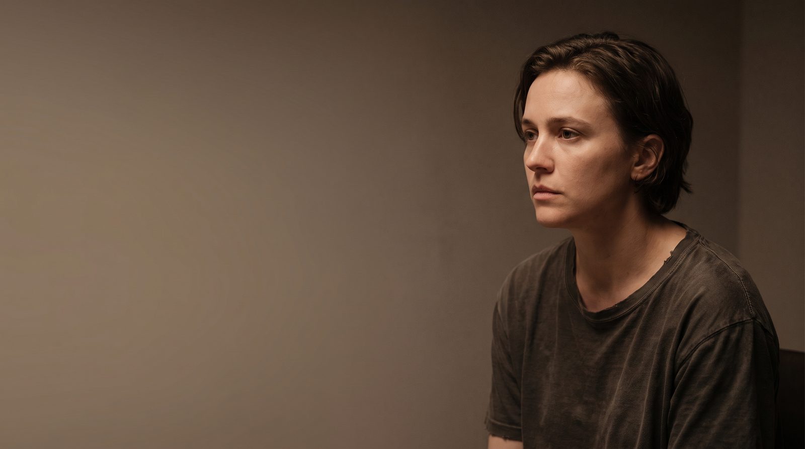 An actor sitting very still in soft light, face filling most of the frame, thinking