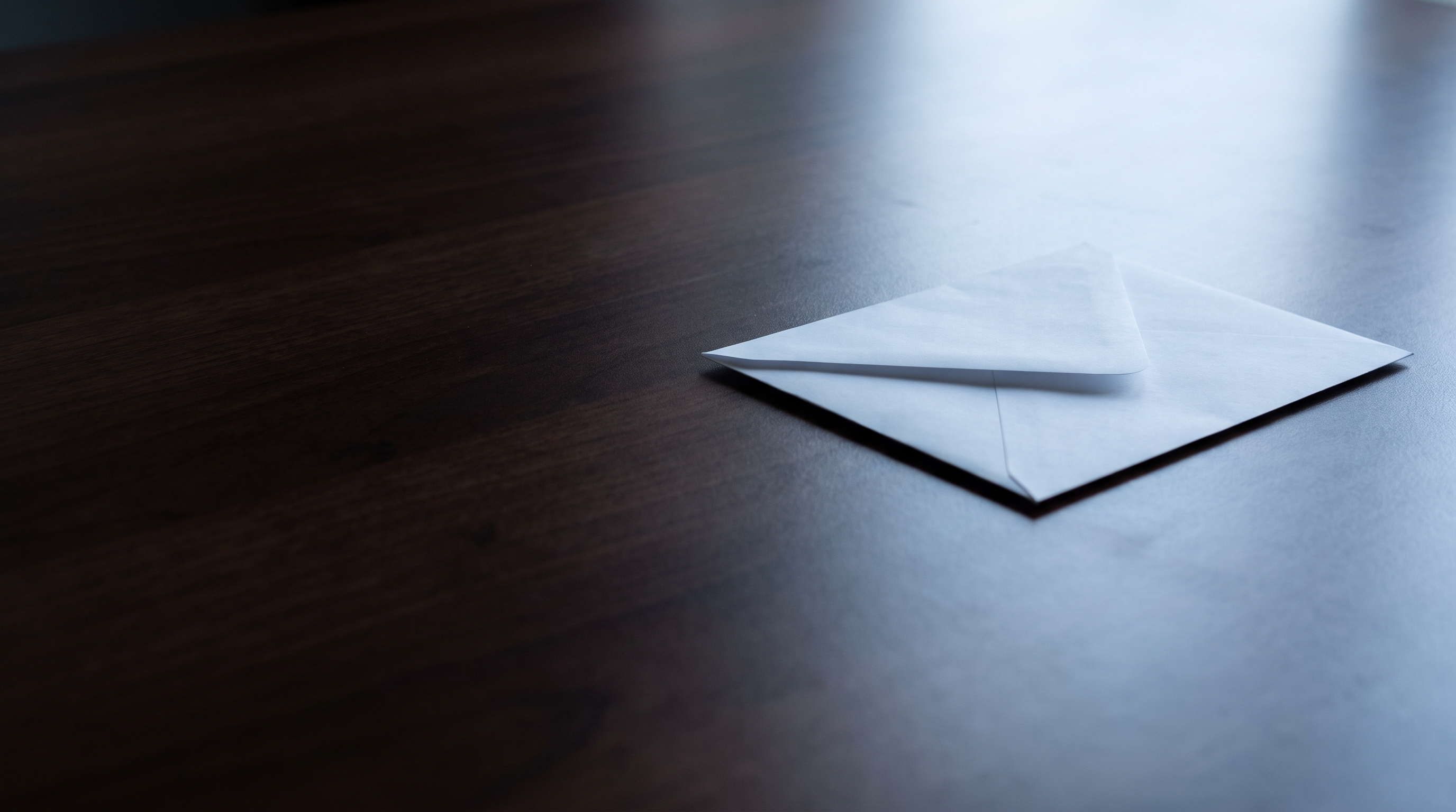 A single blank white envelope lying alone on a dark wooden desk