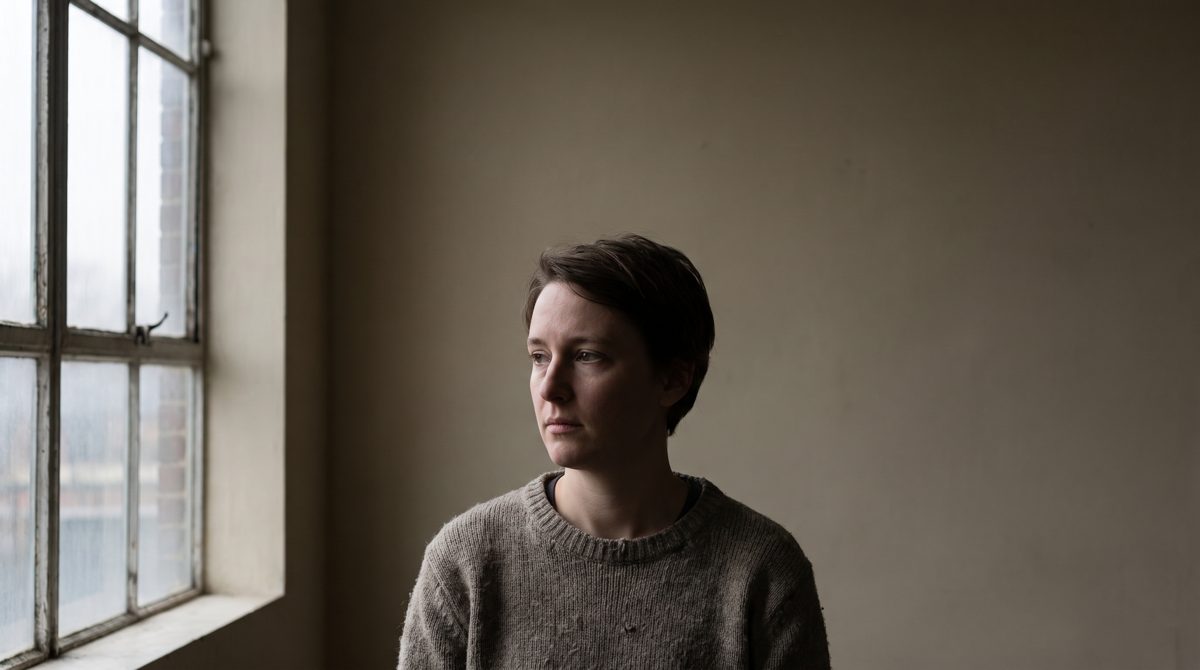 Soft daylight from a large window falling across a person's face in a plain room