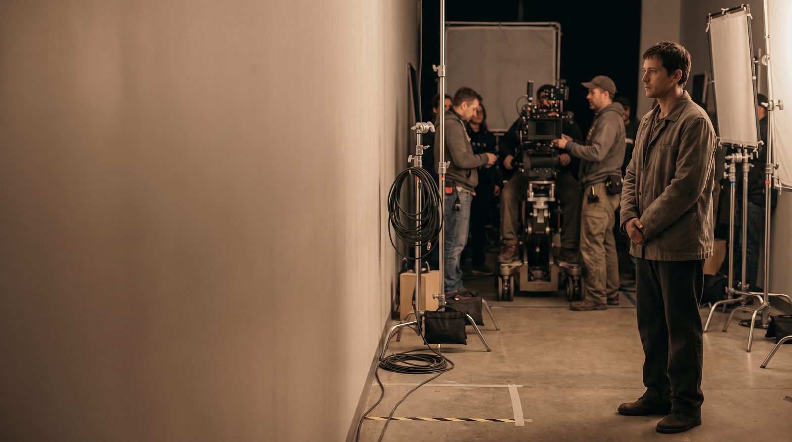 An actor waiting quietly at the edge of a film set while the crew work around a camera