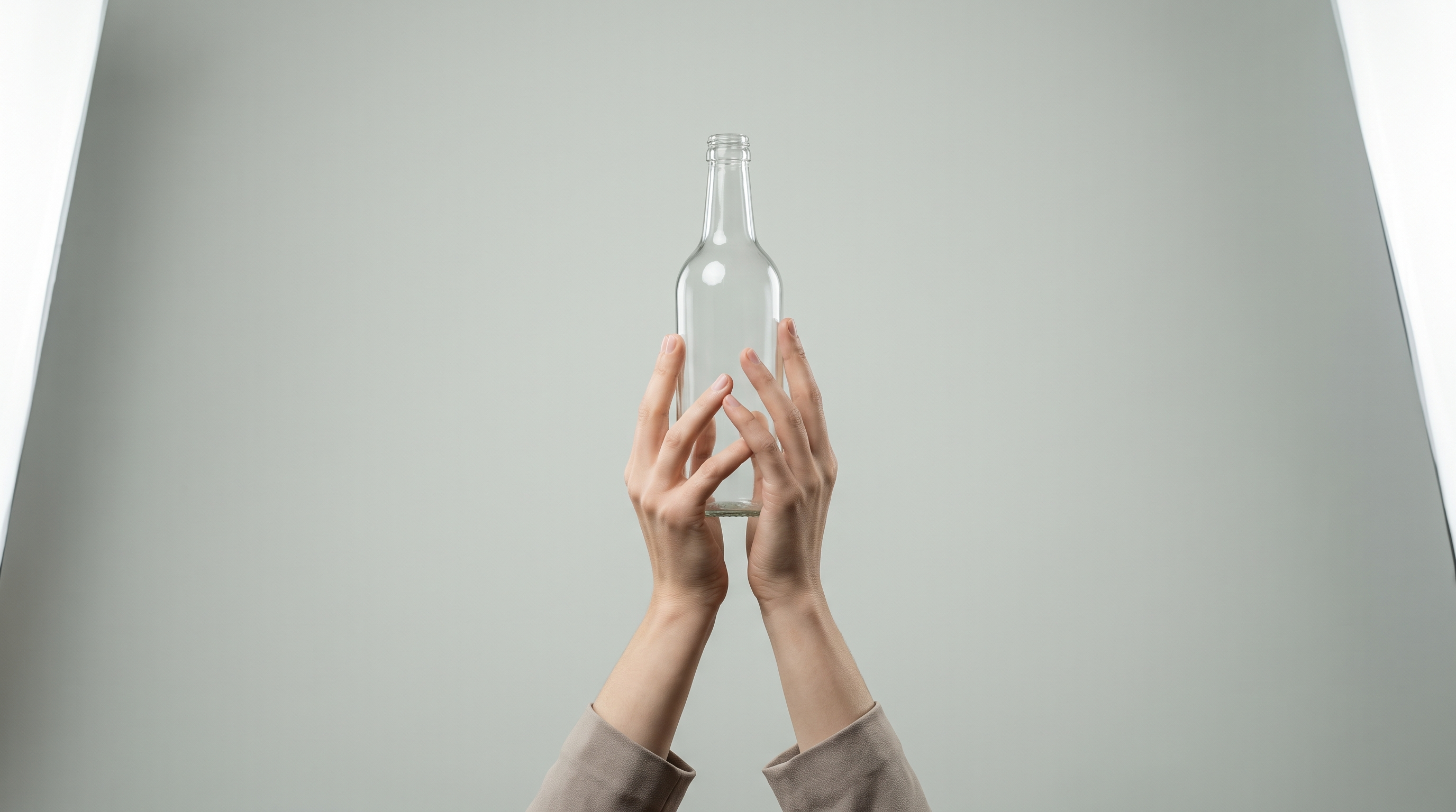 A pair of hands holding a plain unlabelled glass bottle against a studio background
