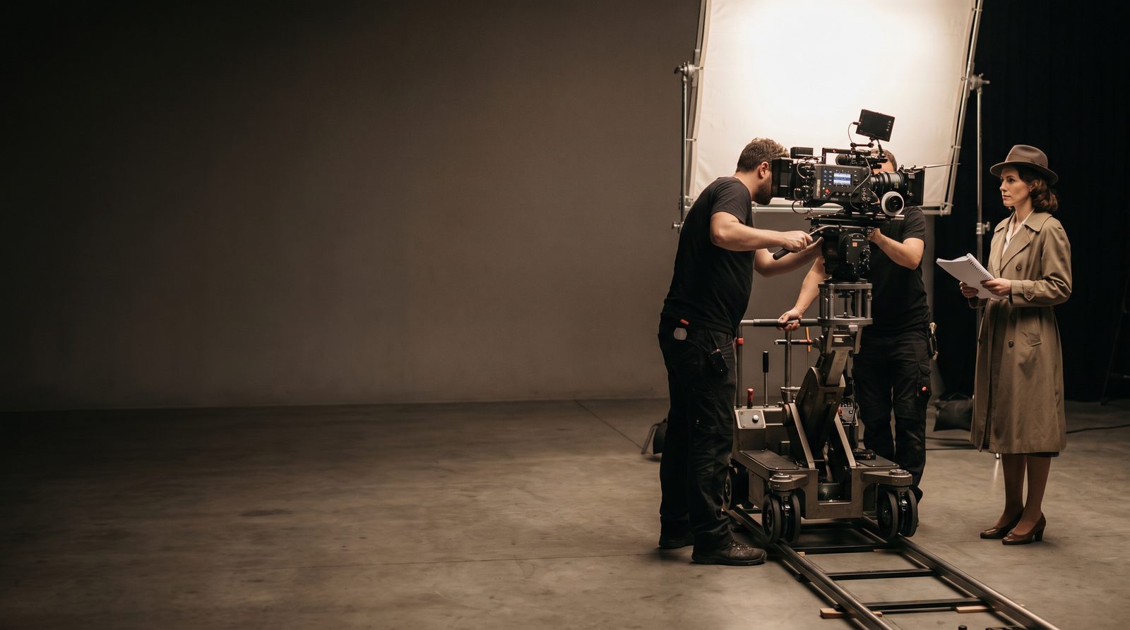 A film crew working around a camera on a set, an actor waiting in the background