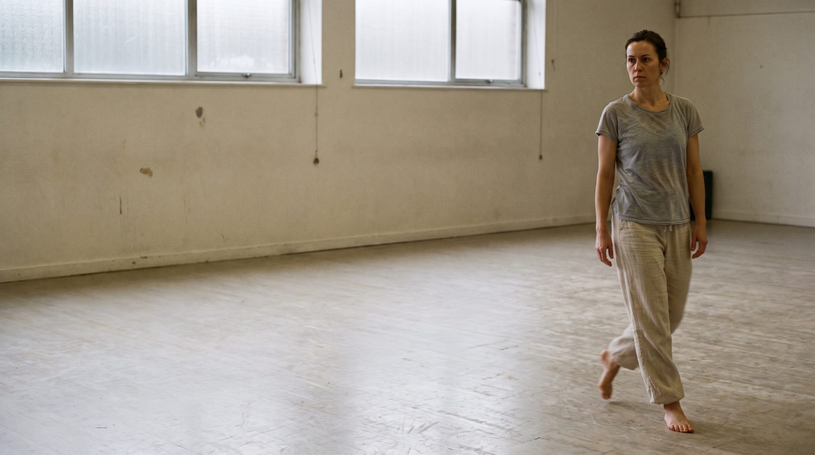 An actor crossing an empty studio floor mid-stride, working on the quality of a walk