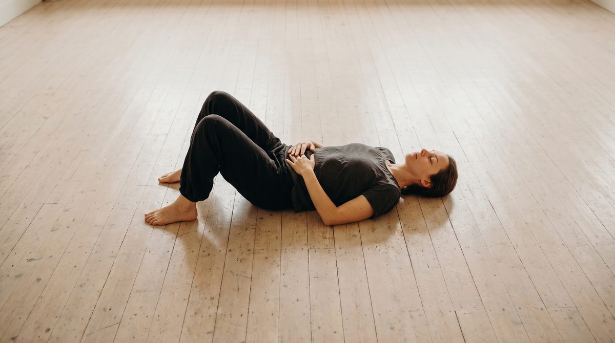 An actor lying on their back on a studio floor, knees bent, hands on the lower ribs