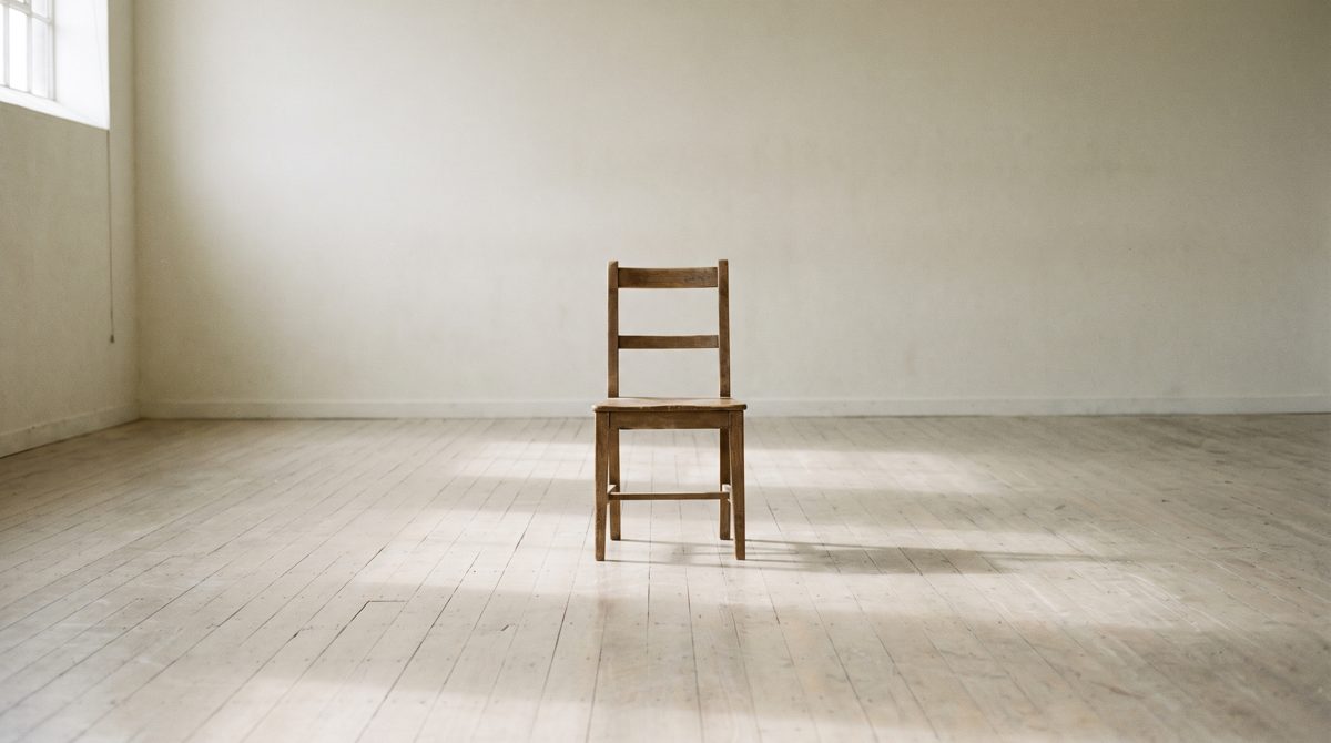 A plain wooden straight-backed chair alone in the middle of an empty rehearsal studio