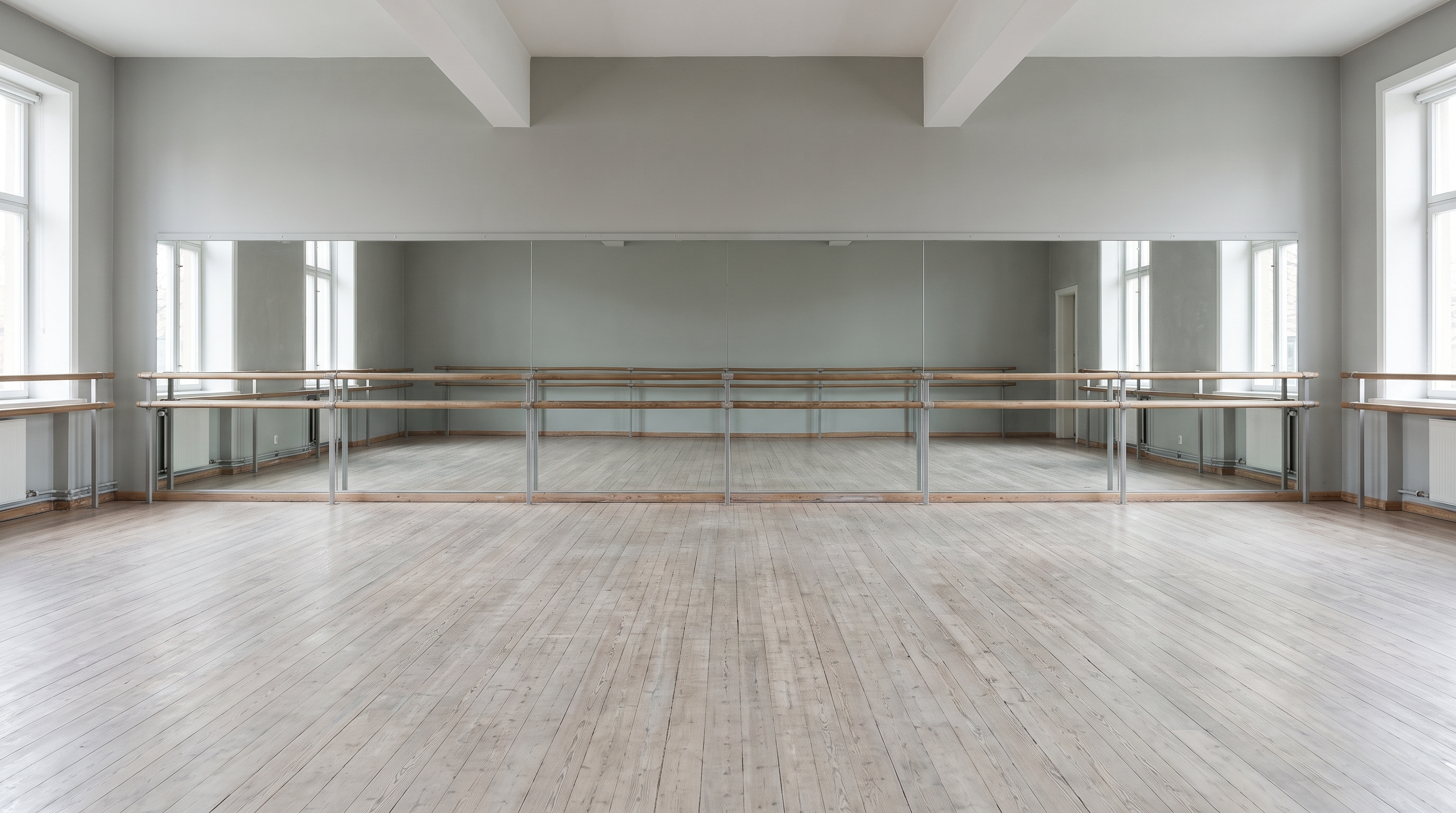 A wooden ballet barre running across an empty dance studio in front of a mirrored wall