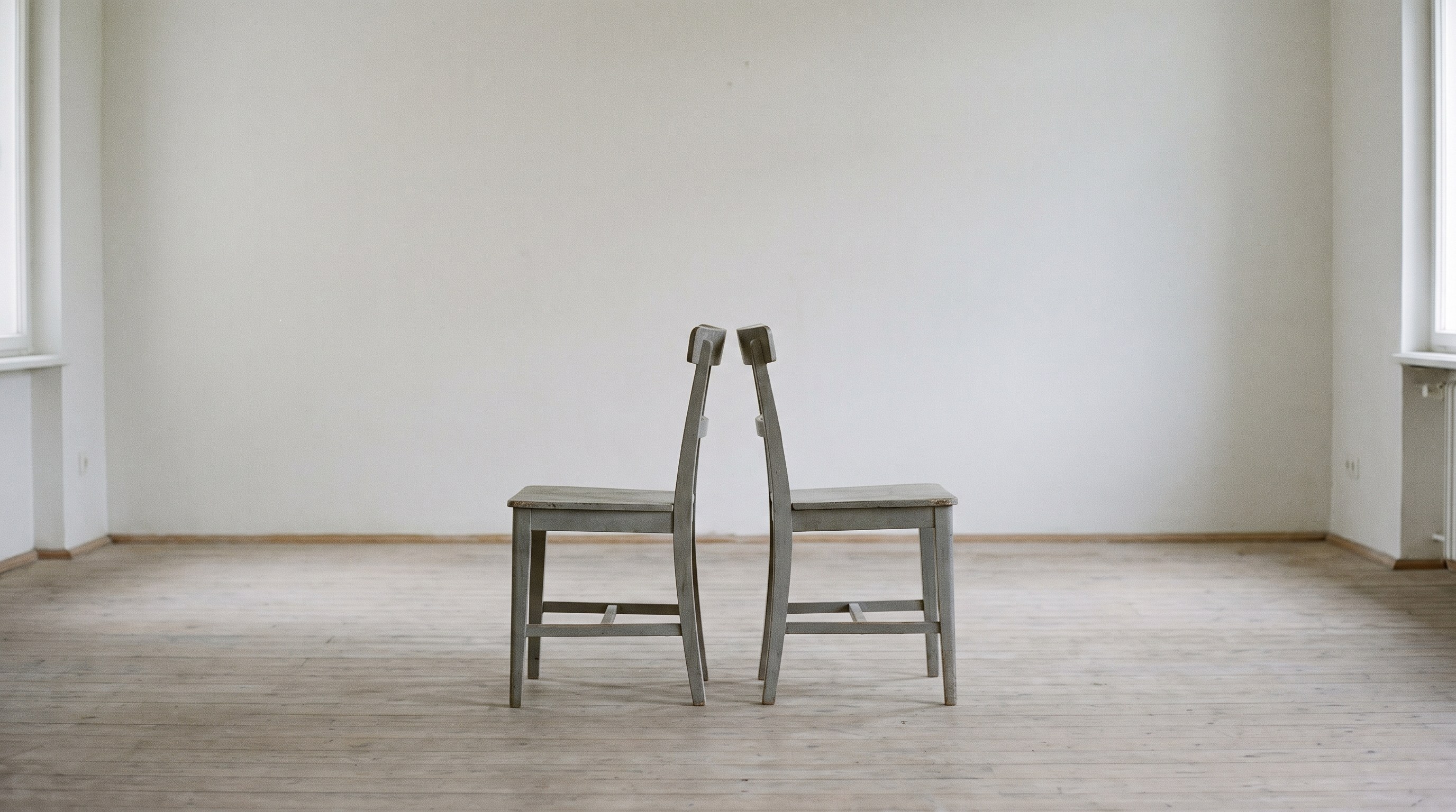 Two plain wooden chairs facing each other in an empty room, both empty
