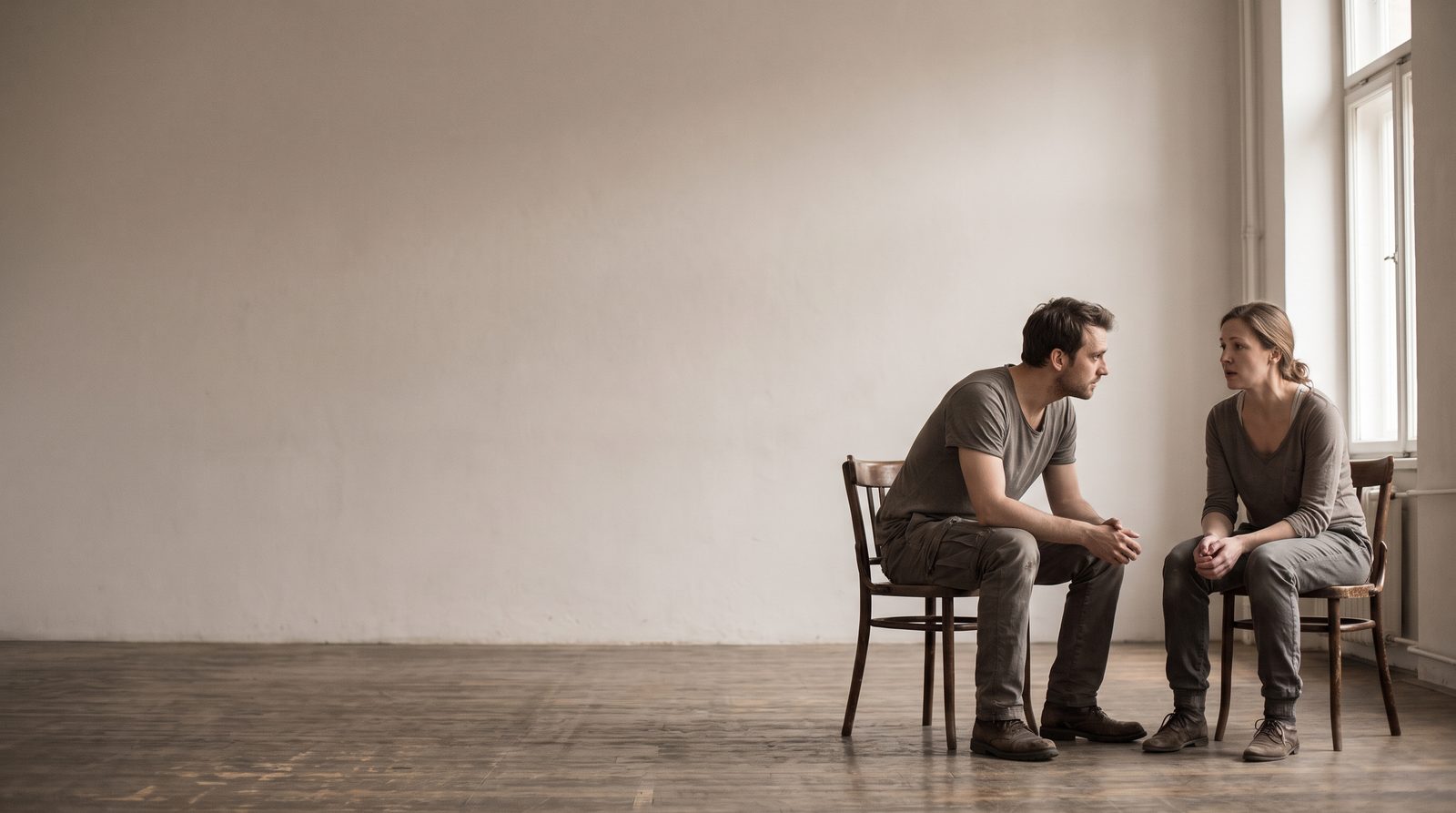Two actors facing each other in a bare rehearsal room, one listening to the other