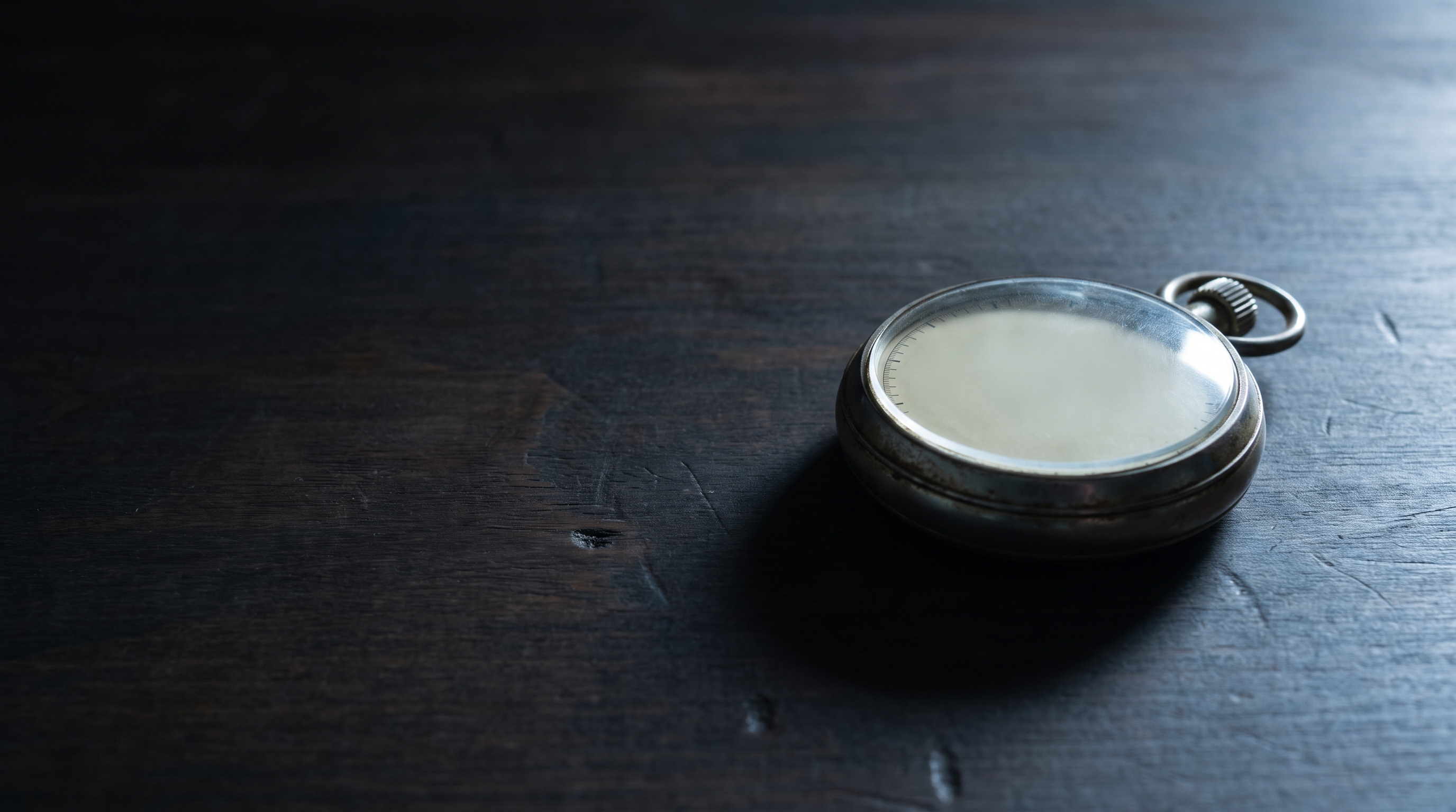 An old mechanical stopwatch with a blank dial lying on a bare wooden desk