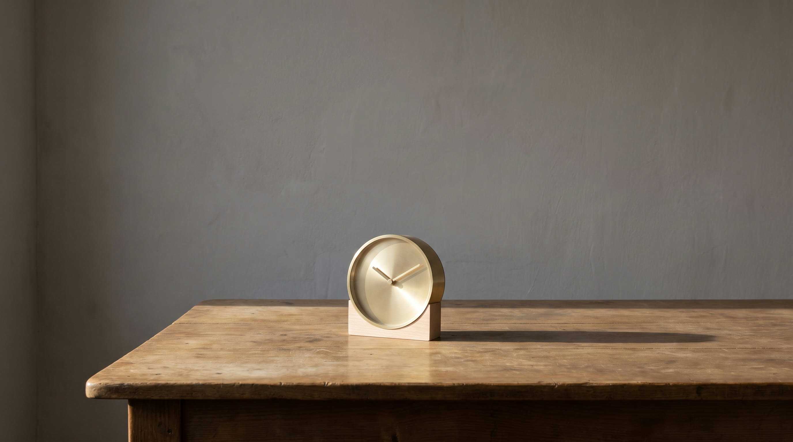 A small plain mantel clock standing alone on a bare wooden table against an undecorated wall