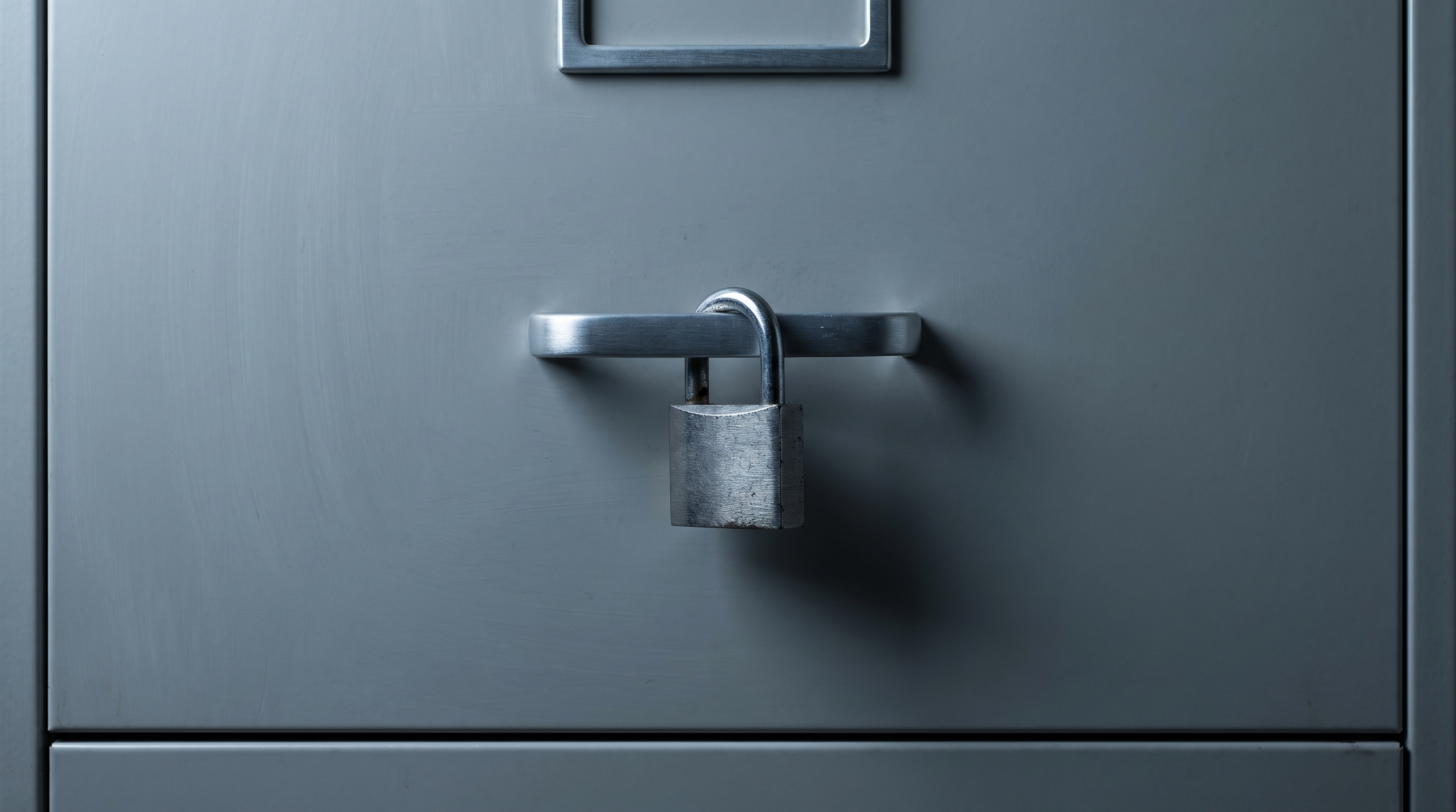 A small steel padlock hanging closed on the handle of a grey metal cabinet
