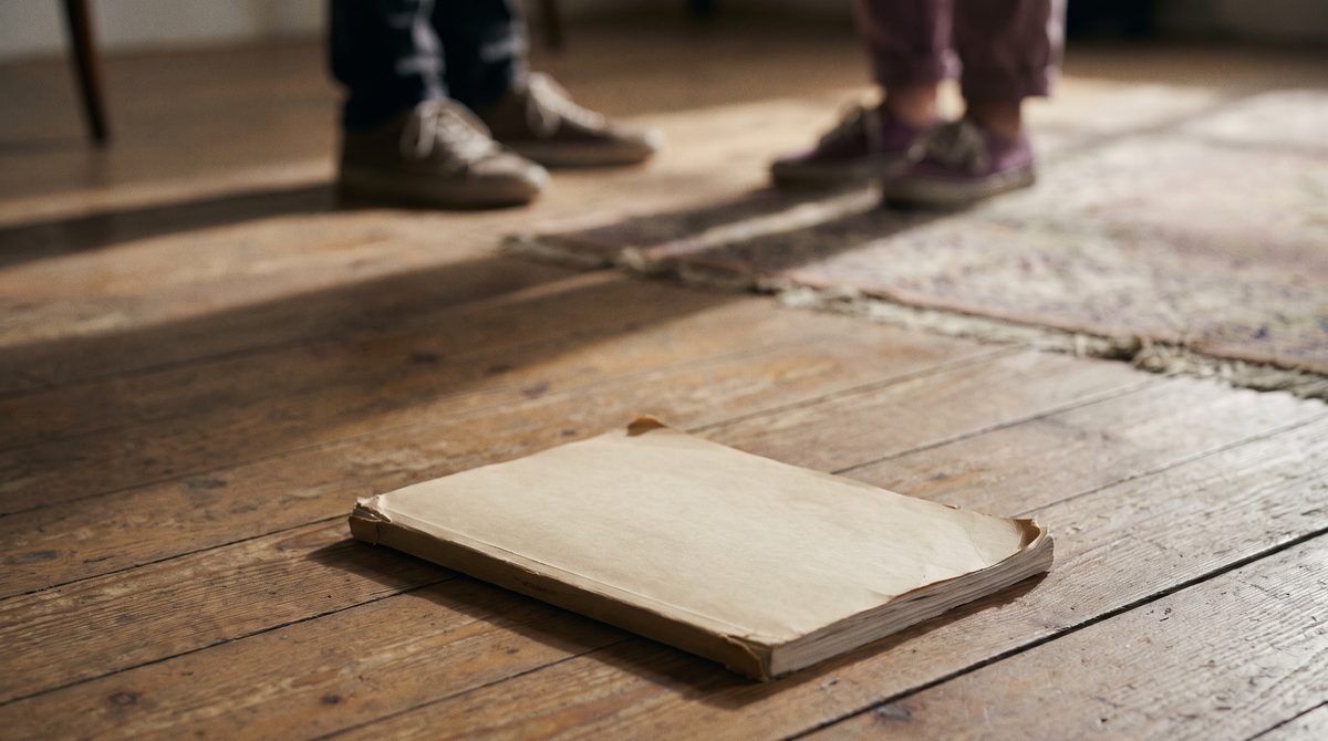 A script abandoned on a rehearsal room floor while two actors work beyond it