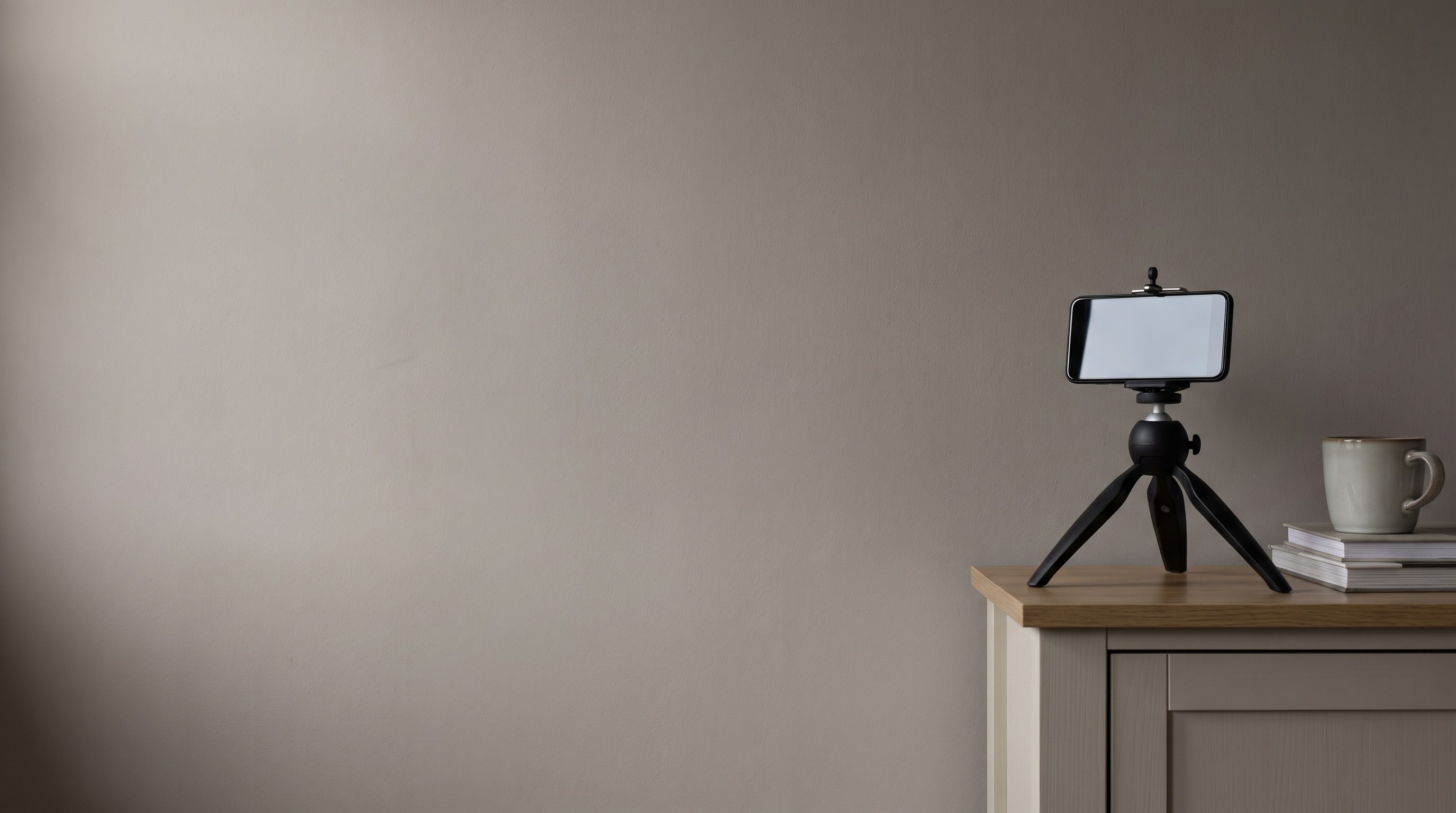 A mobile phone on a small tripod in an ordinary living room, facing a plain pale wall