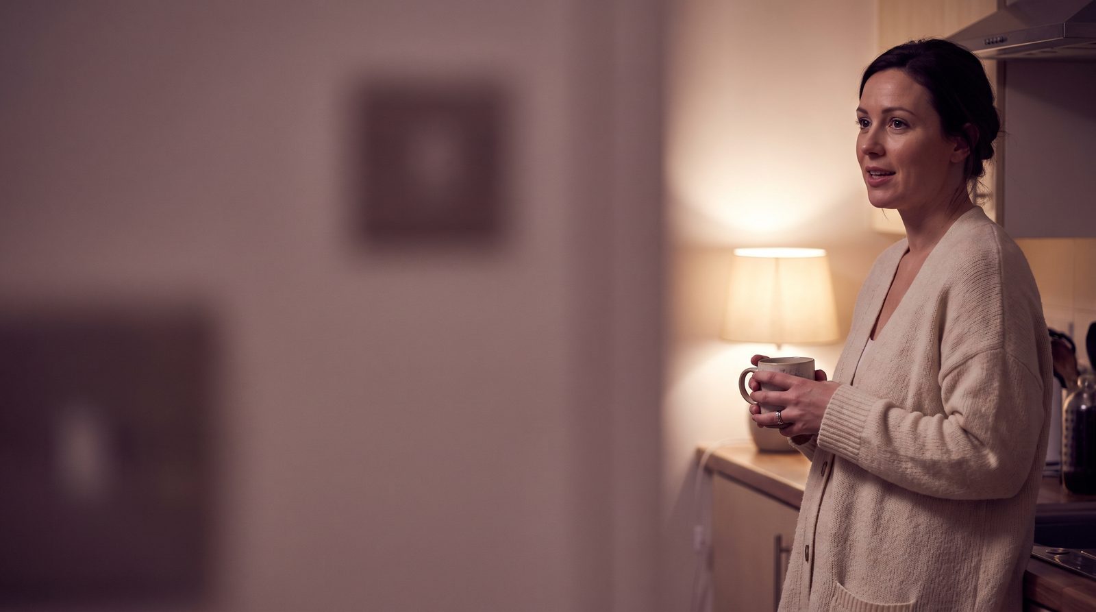 A woman in a kitchen at night, talking about something unimportant