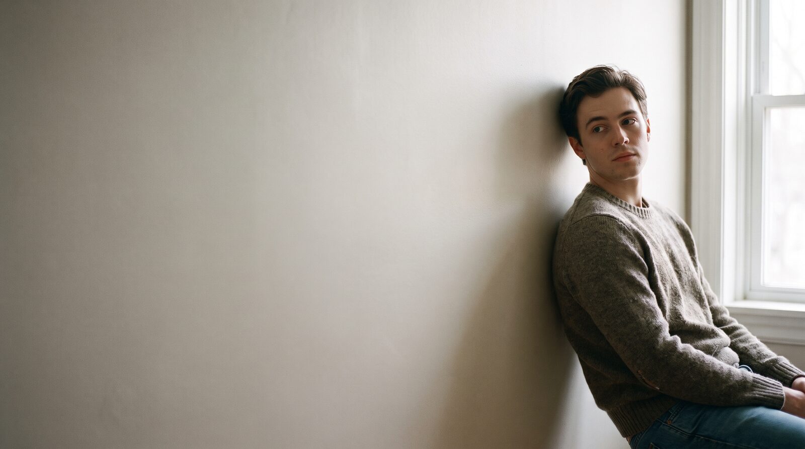 An actor standing in a plain room in an unguarded moment between takes