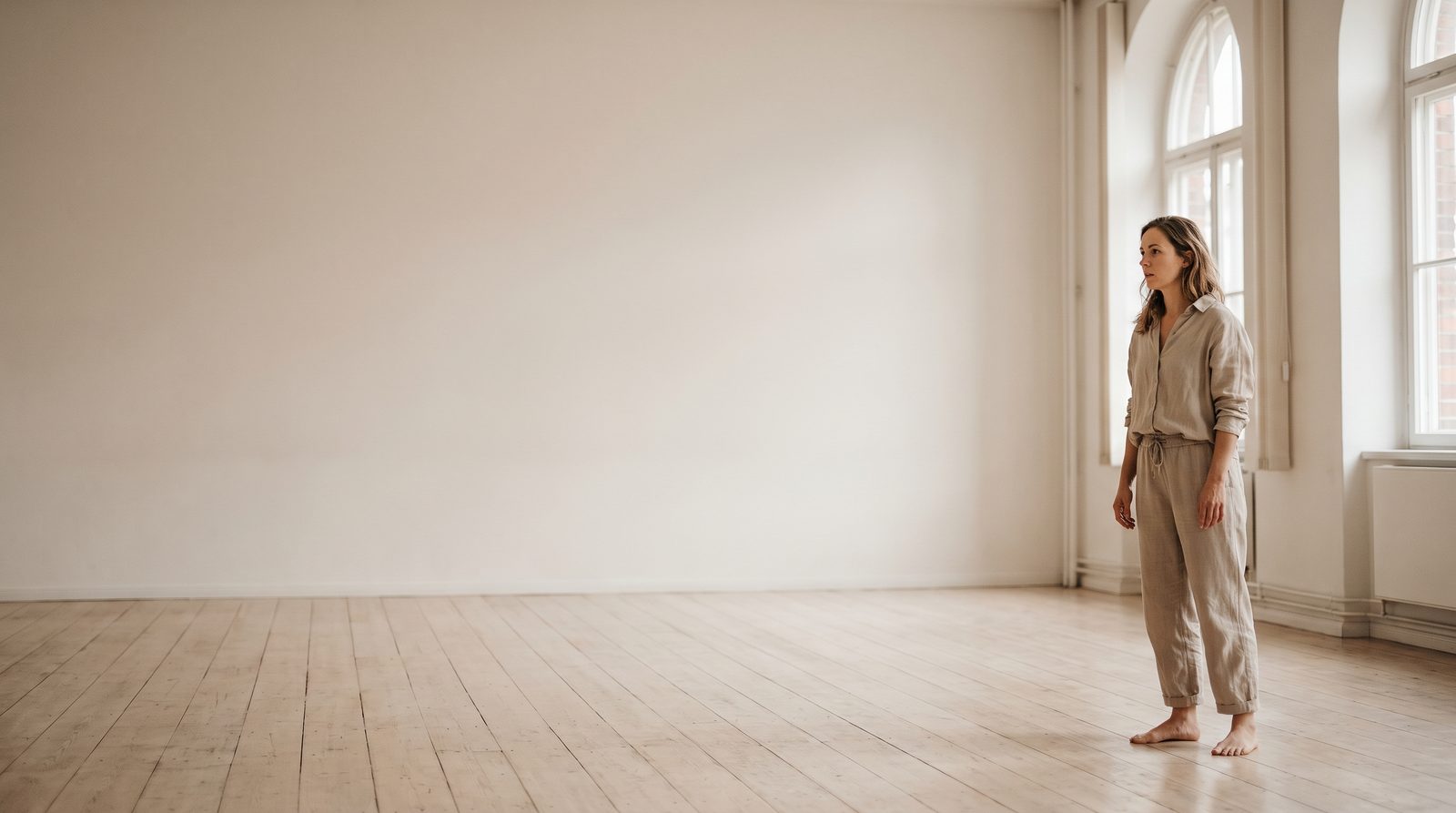 An actor standing still in a large empty studio, attention turned outward into the room