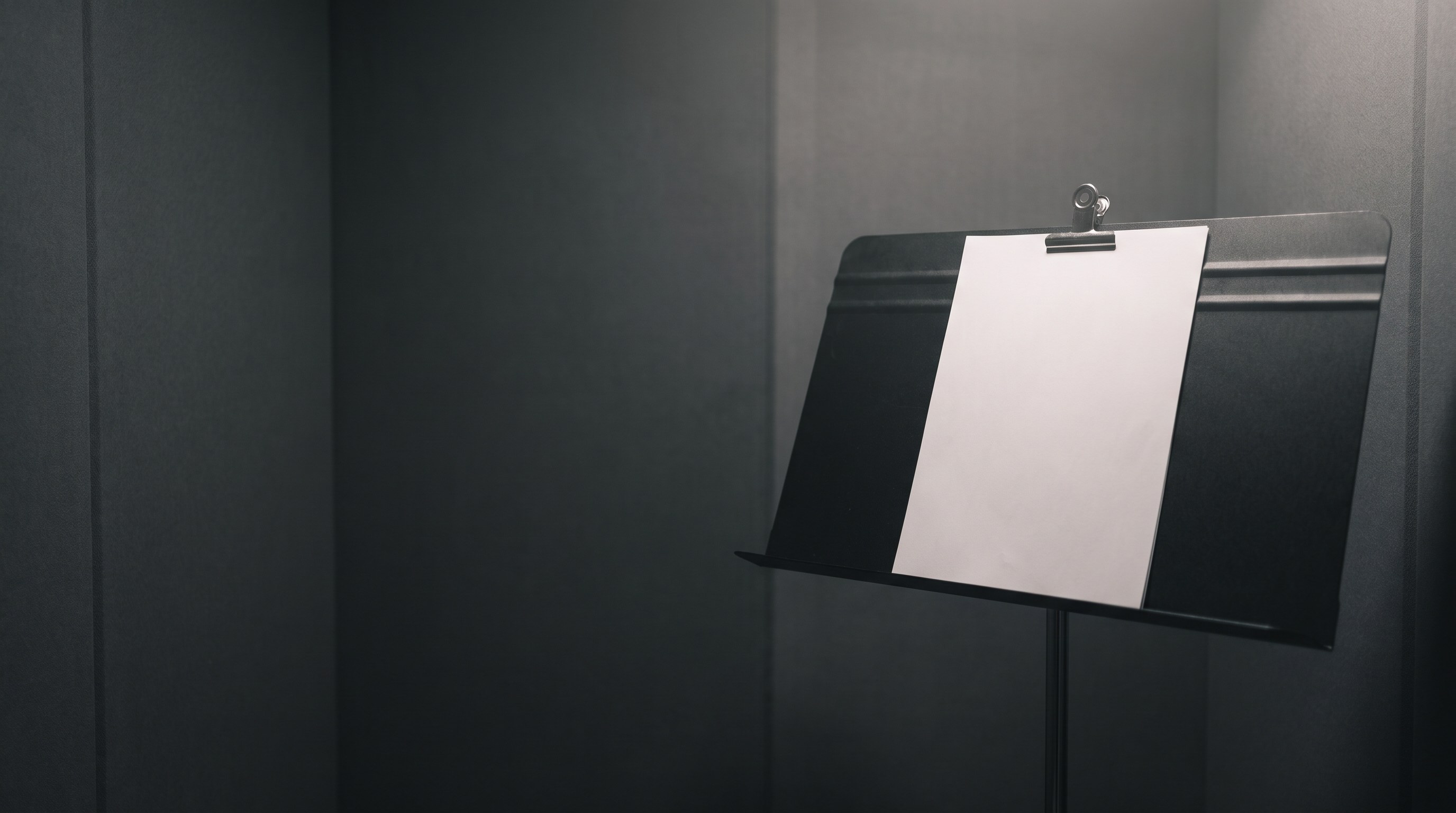 A blank sheet of paper clipped to a music stand in an empty recording booth