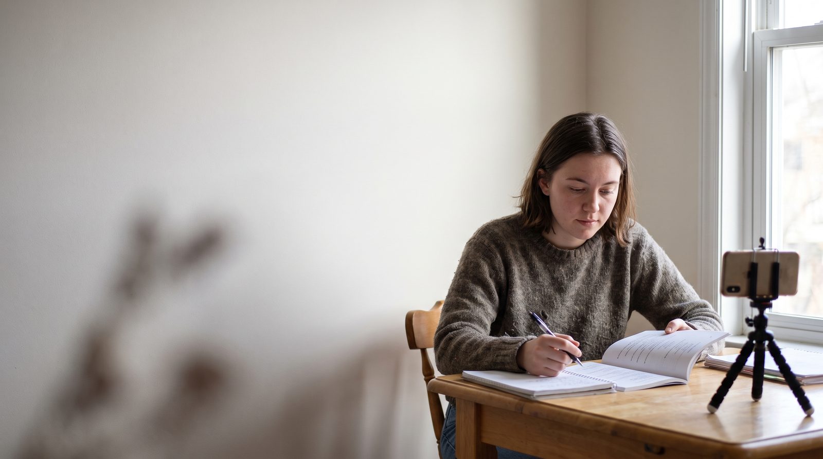A young actor working from a play script at a kitchen table with a phone on a tripod