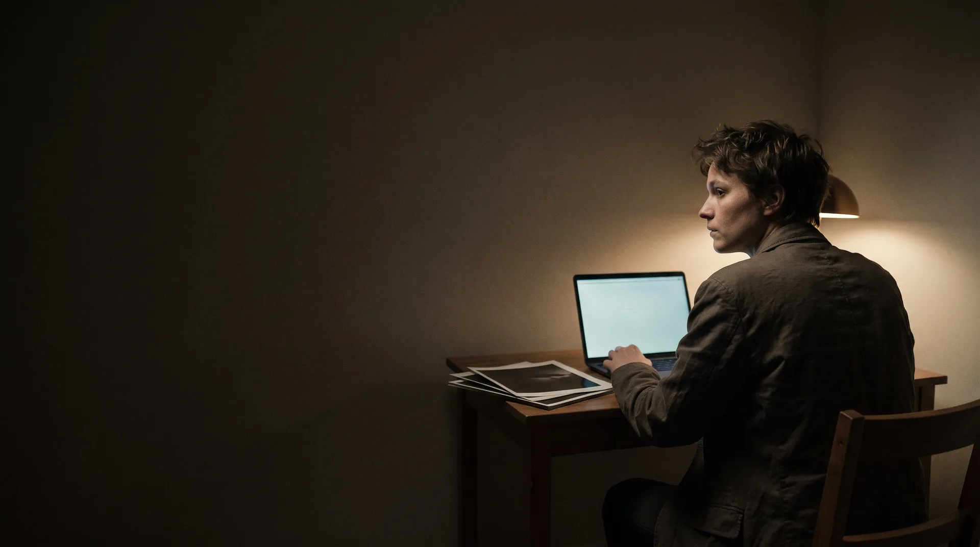 An actor at a desk late at night with a laptop and a stack of prints