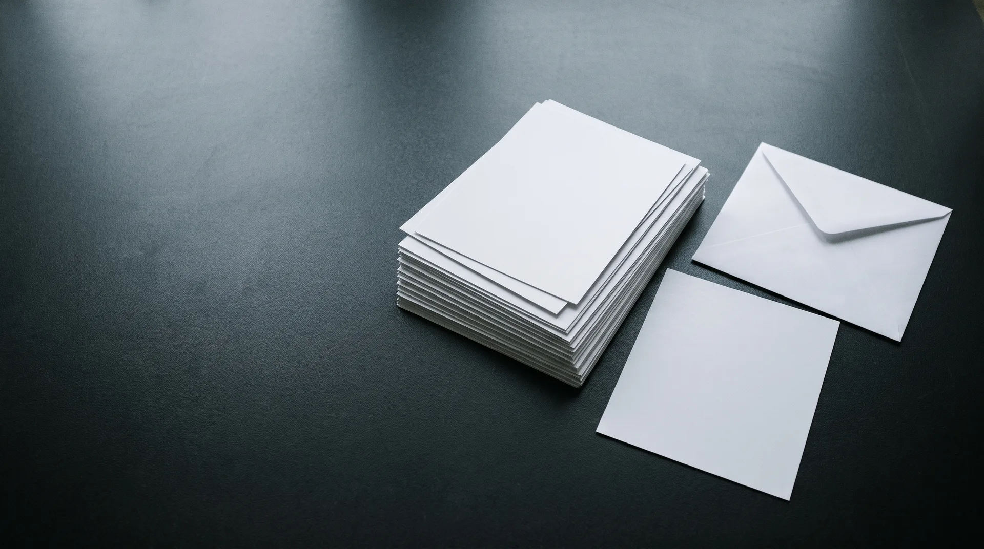 A stack of large photographic prints lying face down on a dark table beside a plain envelope