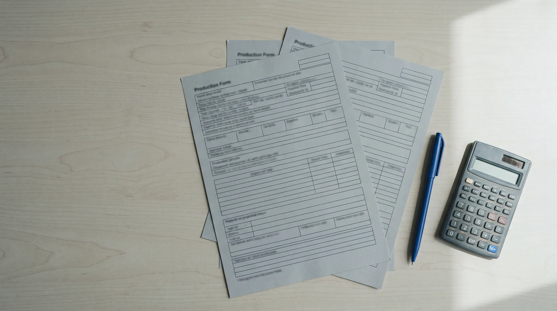 Blank production paperwork, a pen and a pocket calculator on a pale table