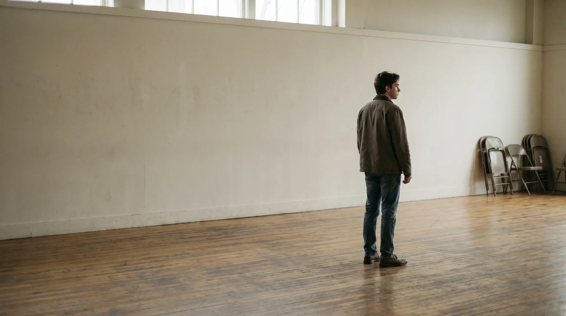 A person standing alone in an empty acting studio, seen from behind