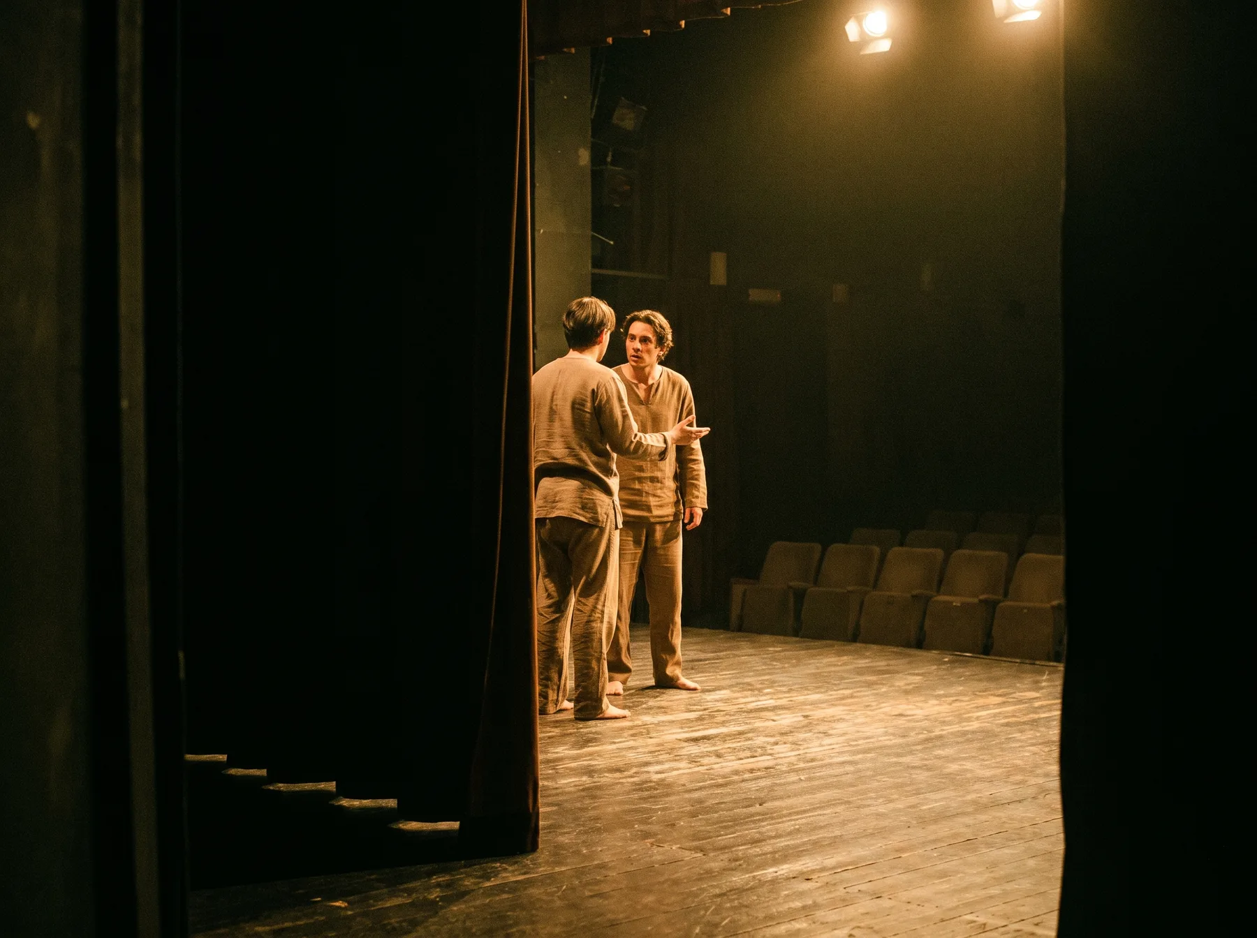 Two actors performing on a small theatre stage seen from the wings