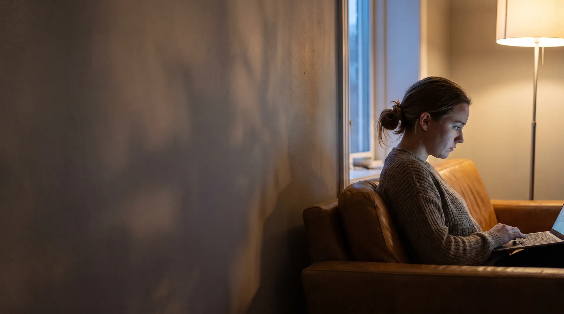 An actor sitting alone in a dim room, reading a message on a laptop