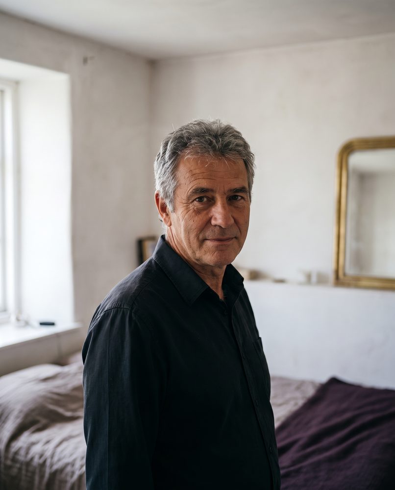 An actor standing against a plain wall, calm and settled, no longer performing