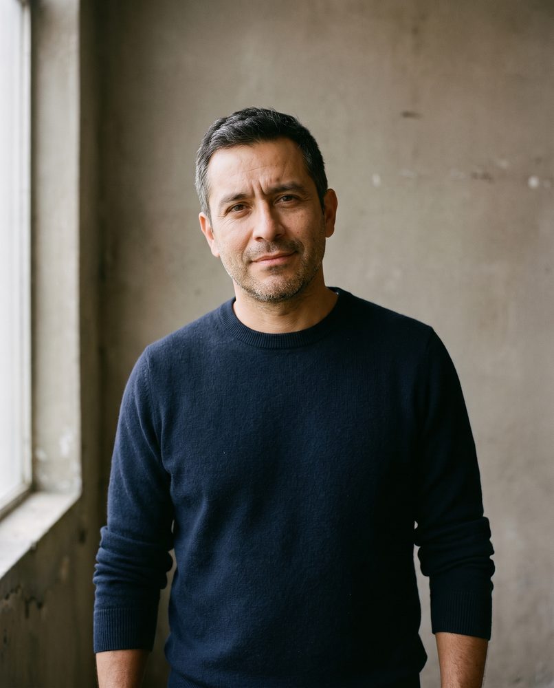 An actor standing against a plain wall, looking directly at the camera