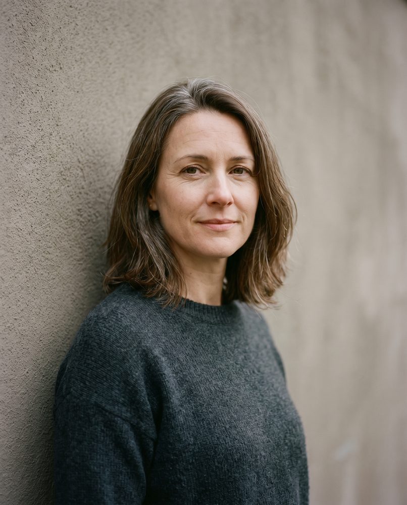 An actor standing against a plain wall, looking directly at the camera